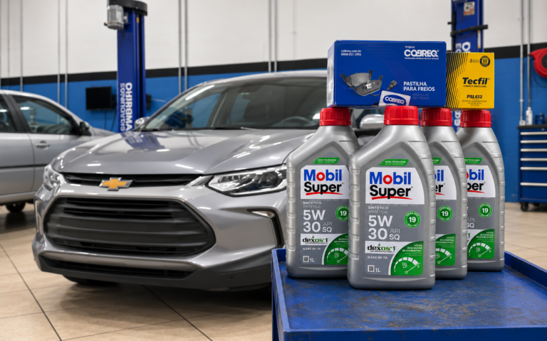 Frascos de óleo de motor sintético, filtro de óleo e pastilhas de freio posicionados em frente a um veículo Chevrolet na Elite Car Centro Automotivo, em Extrema-MG, preparados para o serviço de troca de óleo.
